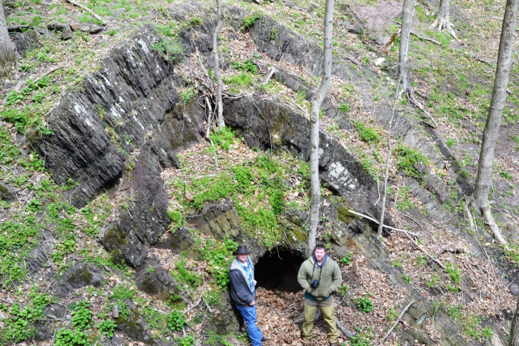 two students stand next to a cave and geological formation