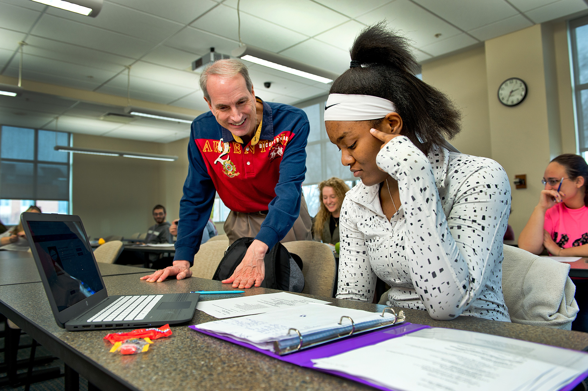 A male professor teaching a female student with a notebook and laptop Spanish