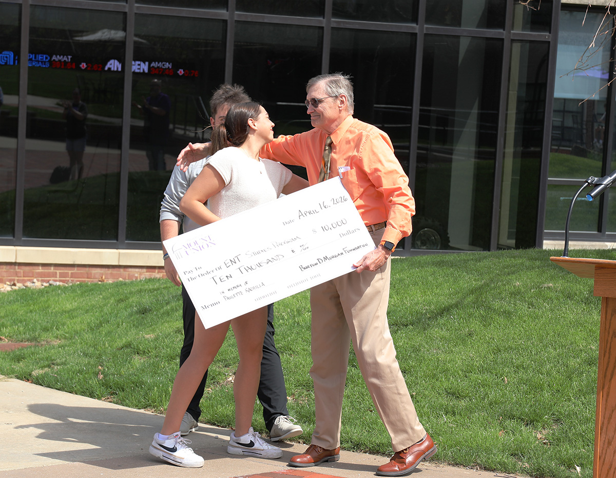 Kachilla hugging students who are presenting him with a check
