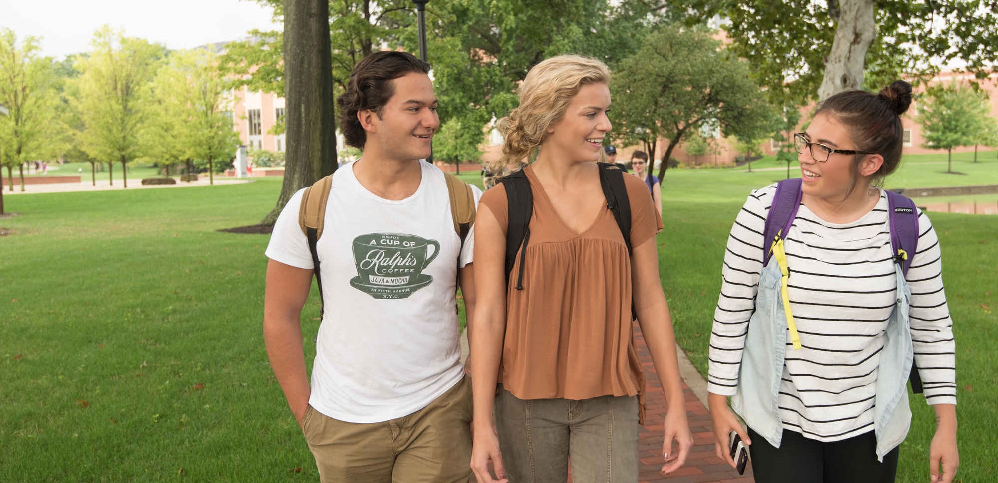 three students walking on sidewalk by campus lakes