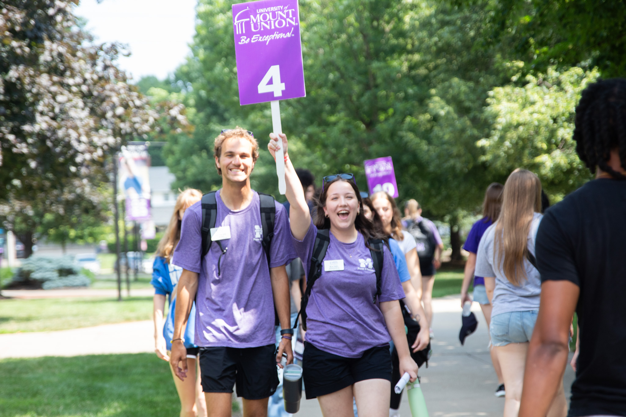 Two preview guides in their purple tshirt and black shorts uniform holding a purple sign with the number 4 on it 