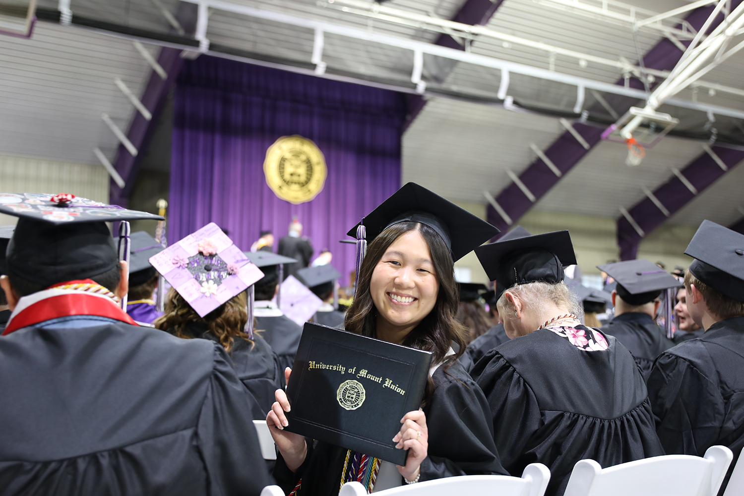 student turned around in the graduation crowd holding a diploma book
