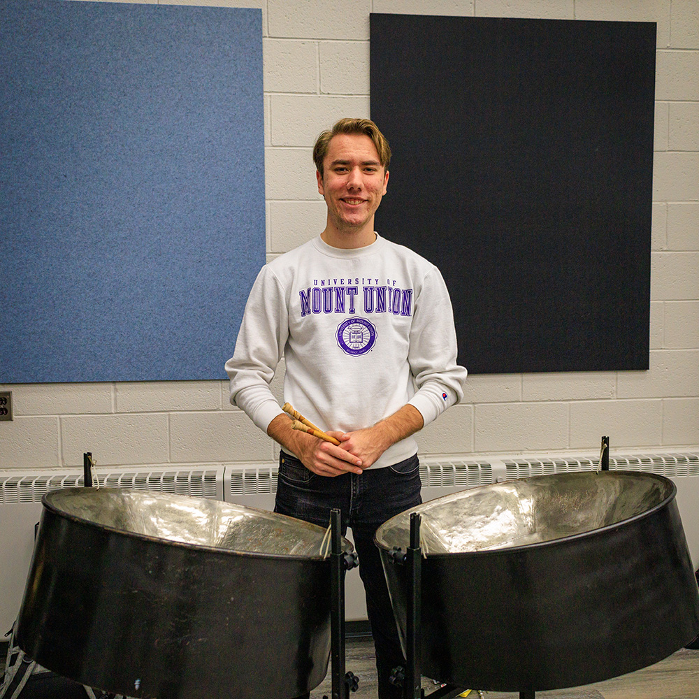 Max Dudack stands wearing Mount Union sweatshirt behind two steel pans